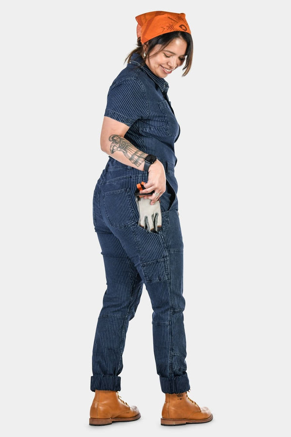 Back view of the Hadley Short Sleeve Coveralls in Dark Blue Wabash Stripe by Dovetail Workwear, featuring reinforced knees and rolled cuffs on a woman wearing an orange cap