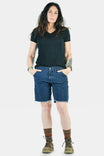 Dovetail Workwear Wabash Work Short in Wabash Stripe with 8-inch inseam, worn by a woman with hands in pockets, paired with a black v-neck tee and hiking boots