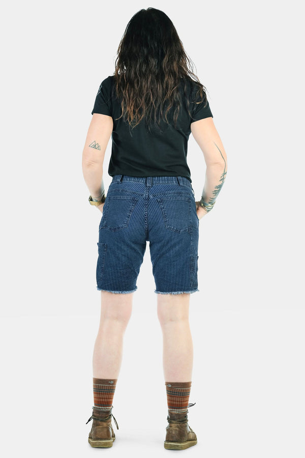 Back view of a woman wearing Dovetail Workwear's Wabash Work Short in Wabash Stripe with an 8-inch inseam, paired with a black tee and patterned socks