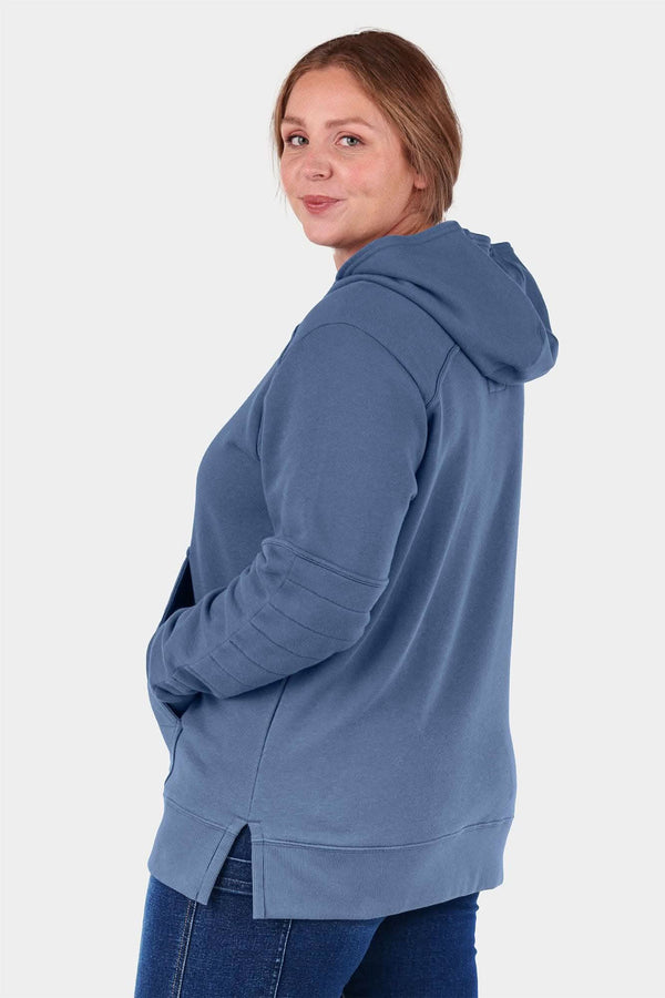 Back view of a woman wearing the John Deere X Dovetail Workwear Early Bird Hoodie in Steel Blue, showcasing the ponytail slit and relaxed fit design