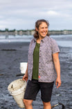 Woman wearing Dovetail Workwear Carver Work Shirt in paprika paisley print with olive tee, holding bucket at beach, smiling at camera