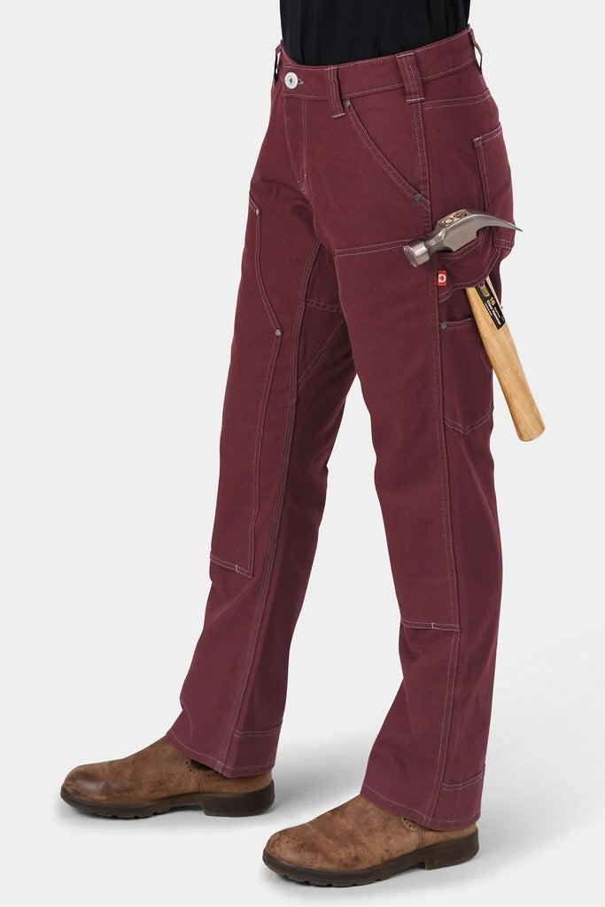 Woman wearing Dovetail Workwear's Anna Taskpant in Elderberry Canvas with a claw hammer in the Hip Slot™ tool loop, showcasing the relaxed-fit work pant's multiple pockets and durable midweight canvas construction