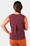 Back view of a woman wearing the Dovetail Workwear Bellows Work Tank Top in Elderberry (Maroon), showcasing the breathable back pleat and loose fit design