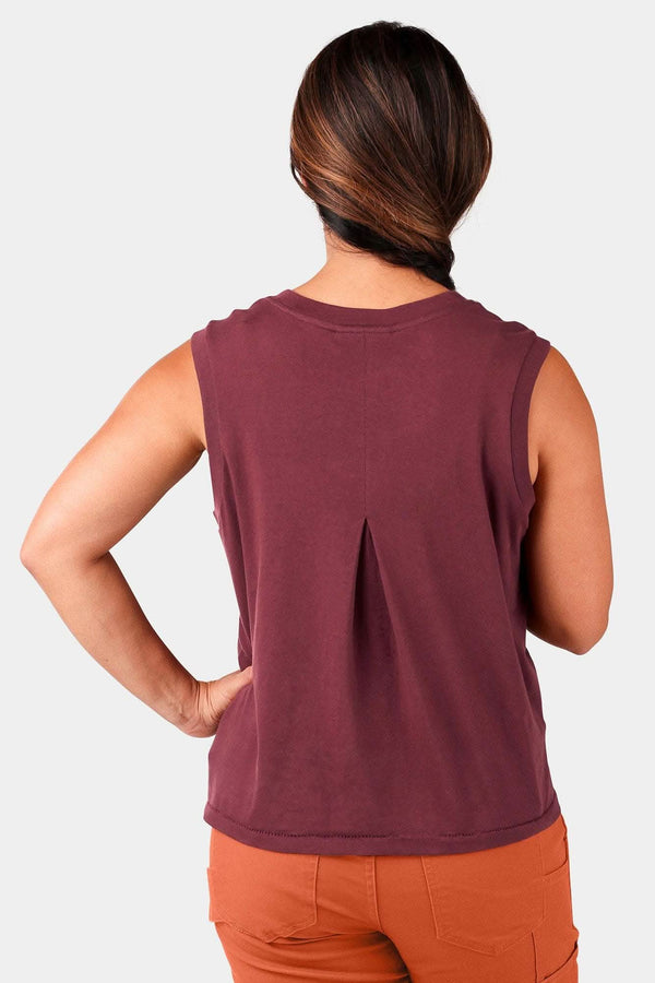 Back view of a woman wearing the Dovetail Workwear Bellows Work Tank Top in Elderberry (Maroon), showcasing the breathable back pleat and loose fit design
