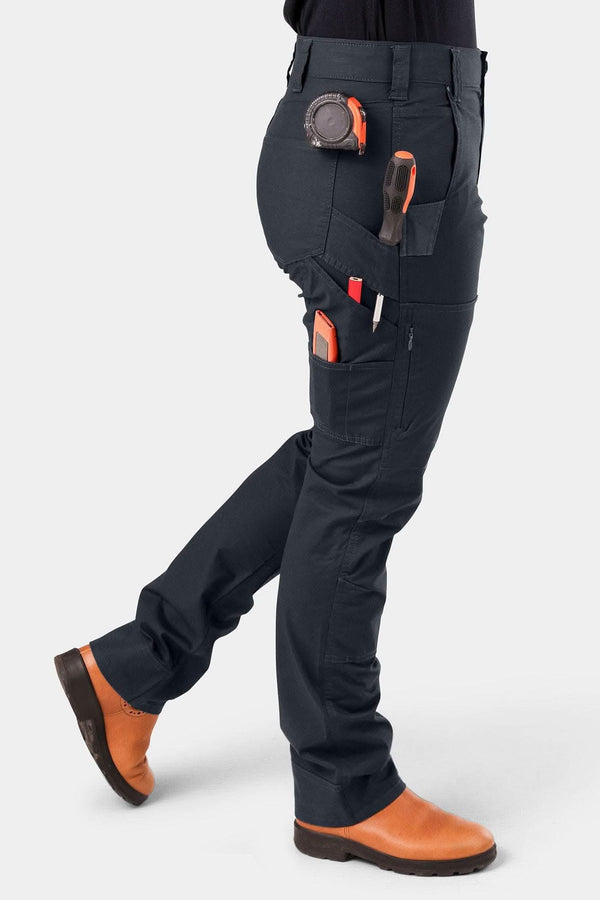 Side view of a woman wearing Dovetail Workwear's Britt X Ultralight Work Pant in Navy Ripstop, showcasing Hip Slot™ cargo pockets, tool loops, and orange boots