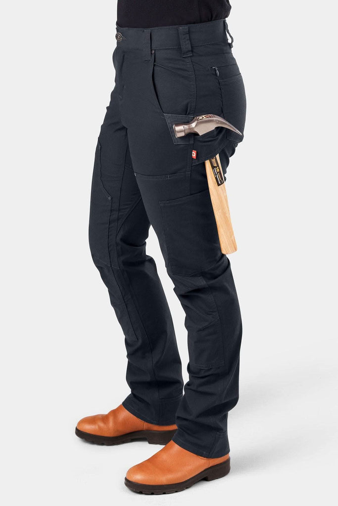 Woman wearing Dovetail Workwear's Britt X Ultralight Work Pant in Navy Ripstop with tool loop and hammer, showcasing zip pockets and straight leg design