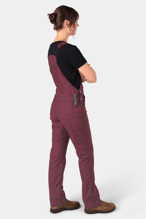 Back view of a woman wearing Dovetail Workwear's Freshley Overalls in Ultralight Ripstop in Elderberry Maroon with a black t-shirt, showcasing the flex suspenders and nested pockets.