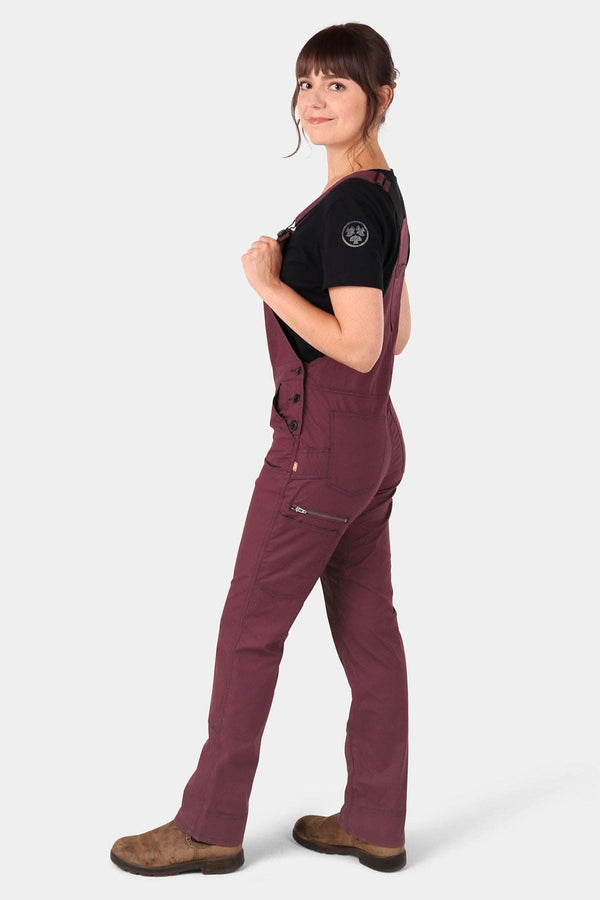 Side view of a woman wearing Dovetail Workwear's Freshley Overalls in Ultralight Ripstop in Elderberry Maroon with a black t-shirt, featuring visible hip pockets and a relaxed leg fit