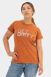 Woman wearing Dovetail Workwear's Get Dirty™ Crew Neck T-Shirt in Paprika with white graphic text, paired with blue jeans
