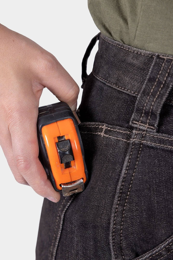 Woman holding an orange utility tool at the Hip Slot™ of Dovetail Workwear's Old School High Rise Graphene Denim Pant in Heather Black