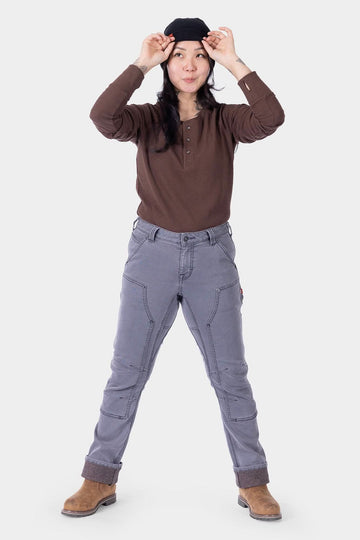 Woman wearing Dovetail Workwear Britt Utility HOTSWAP™ Pant in Grey Thermal Denim with brown henley and black beanie, standing with legs apart to showcase the straight-leg cargo-style pants