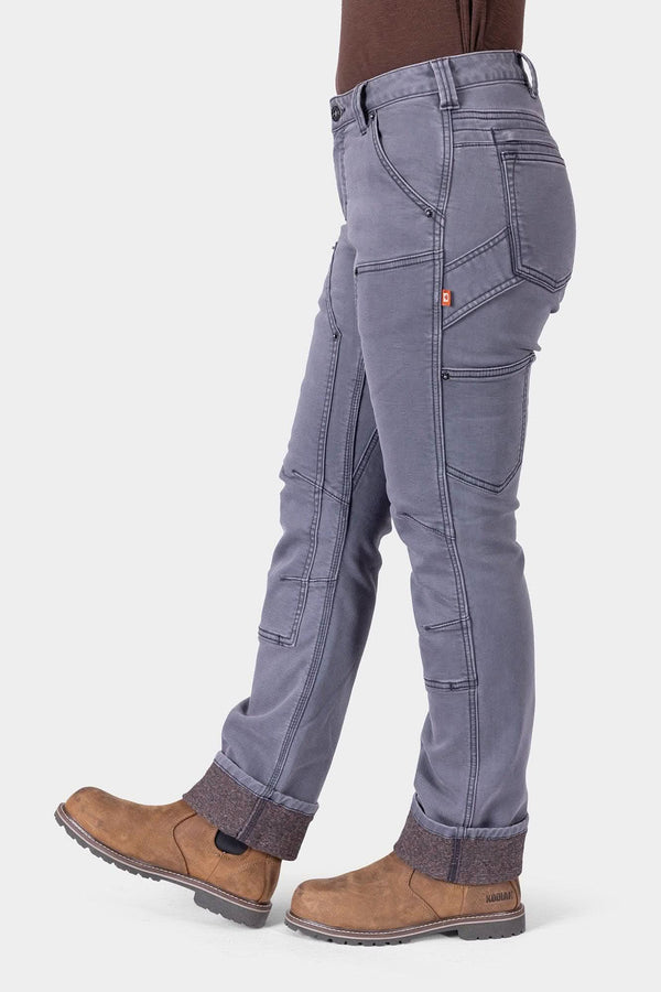 Side view of a woman wearing Dovetail Workwear Britt Utility HOTSWAP™ Pant in Grey Thermal Denim, showcasing cargo pockets, Crotch Gusset, and straight leg fit with brown boots