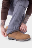 Detail view of a woman adjusting the cuff of Dovetail Workwear's Britt Utility HOTSWAP™ Pant in Grey Thermal Denim, paired with a brown work boot