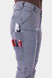 Side view of a woman wearing Dovetail Workwear's Britt Utility HOTSWAP™ Pant in Grey Thermal Denim, displaying multiple cargo pockets with tools and a phone pocket