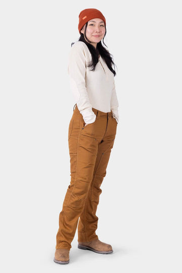 Woman wearing Dovetail Workwear Britt Utility HOTSWAP™ Pant in Saddle Brown Thermal Denim with cream long-sleeve top and rust beanie, showcasing tool loop and straight-leg fit