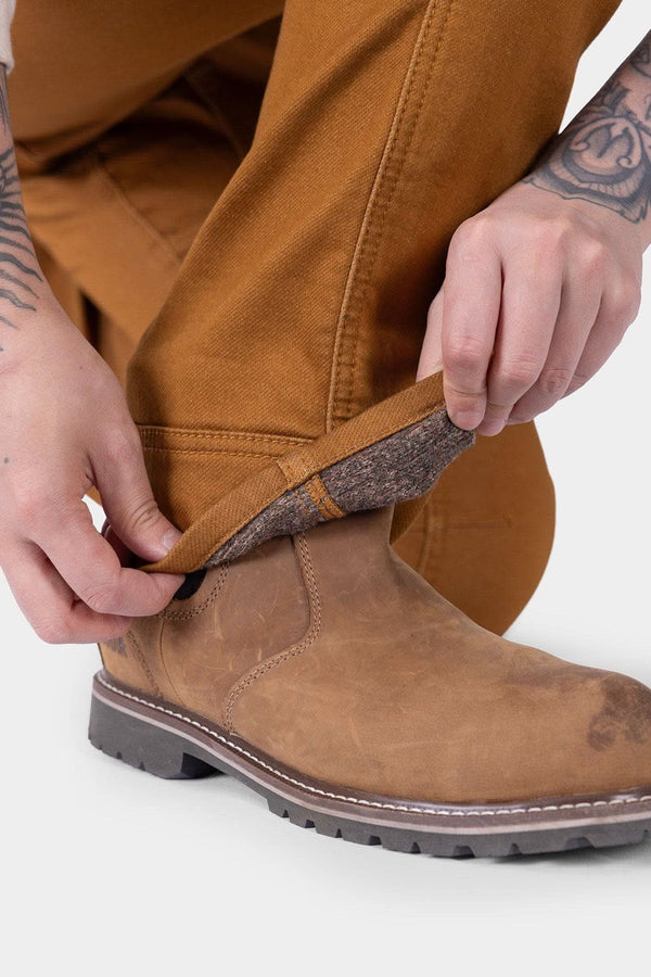 Detail view of a woman adjusting the tool loop on the Britt Utility HOTSWAP™ Pant in Saddle Brown Thermal Denim by Dovetail Workwear, paired with a brown work boot