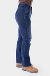 Side view of a woman wearing Dovetail Workwear's Britt X Graphene Denim Pant in indigo, showcasing cargo-style pockets and straight leg fit with brown work boots