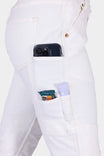 Side view of a woman wearing Dovetail Workwear's GO TO™ Stretch Canvas Work Pant in Painter's White, showcasing multiple functional pockets holding a smartphone, wallet, and sunscreen
