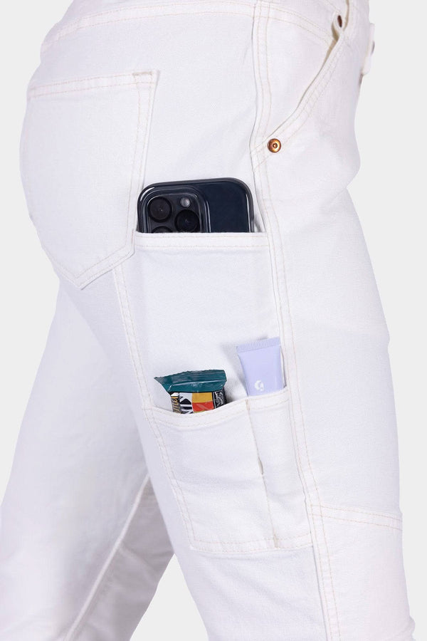 Side view of a woman wearing Dovetail Workwear's GO TO™ Stretch Canvas Work Pant in Painter's White, showcasing multiple functional pockets holding a smartphone, wallet, and sunscreen