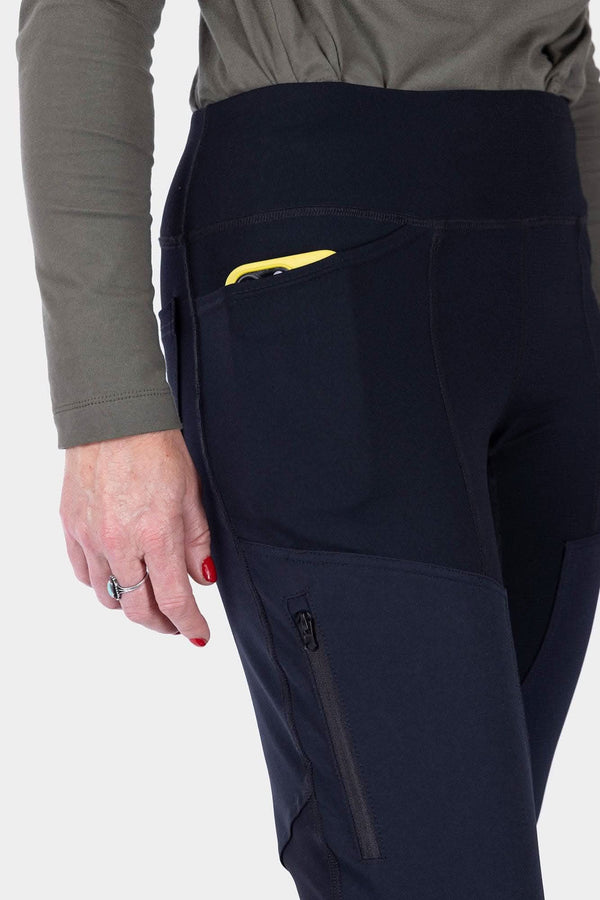 Side view of a woman wearing Dovetail Workwear's Field Utility Legging in Black, highlighting the zip side pocket and fitted silhouette