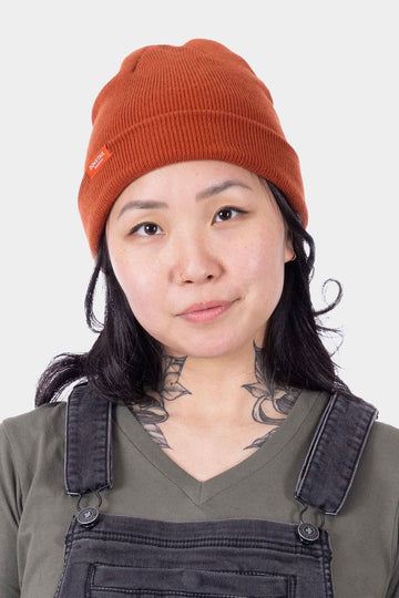 Dovetail Beanie in Paprika worn cuffed by a woman, showing the soft acrylic knit construction and front Dovetail logo detail against a neutral background