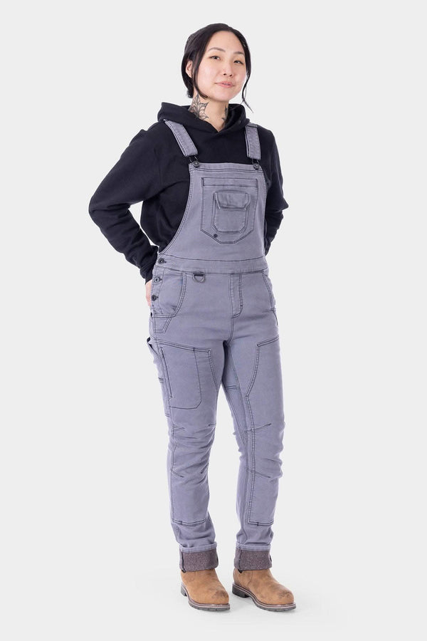 Freshley HOTSWAP™ Drop Seat Thermal Denim Overalls in grey by Dovetail Workwear, worn by a woman with black hoodie and brown boots, front view