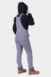 Back view of a woman wearing Dovetail Workwear's Freshley HOTSWAP™ Drop Seat Thermal Denim Overalls in Black with brown work boots, showcasing the reinforced knees and straight leg fit