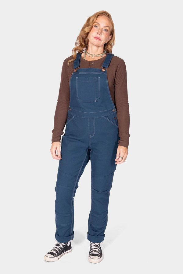 Atlantic Blue GO TO™ Stretch Canvas Overalls by Dovetail Workwear worn with a brown long-sleeve shirt and black sneakers, shown full length on a woman