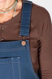 Detail shot of the GO TO™ Stretch Canvas Overalls in Atlantic Blue by Dovetail Workwear, showing the adjustable flex suspender on a woman wearing a brown cardigan