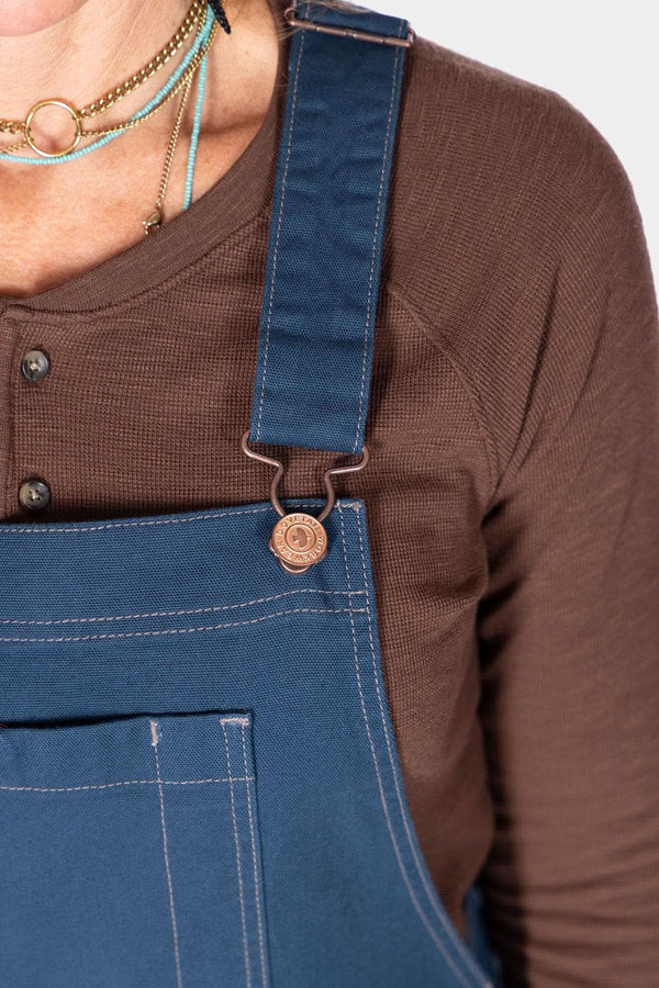 Detail shot of the GO TO™ Stretch Canvas Overalls in Atlantic Blue by Dovetail Workwear, showing the adjustable flex suspender on a woman wearing a brown cardigan