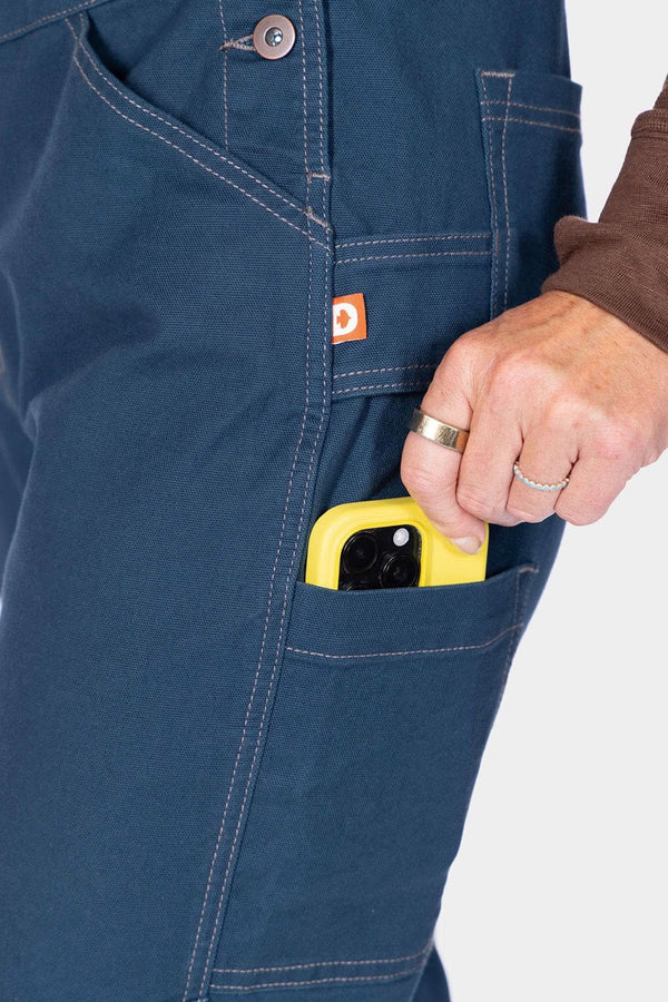 Detail shot of the Atlantic Blue GO TO™ Stretch Canvas Overalls by Dovetail Workwear, highlighting the reinforced knee and phone pocket with a yellow device visible