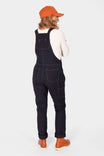 Back view of a woman wearing Dovetail Workwear GO TO™ Stretch Canvas Overalls in Carbon Black with rolled inseam, orange cap and boots