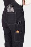 Back view of a woman wearing Dovetail Workwear GO TO™ Stretch Canvas Overalls in Carbon Black, displaying multiple pockets and work gloves stored in the chest pocket