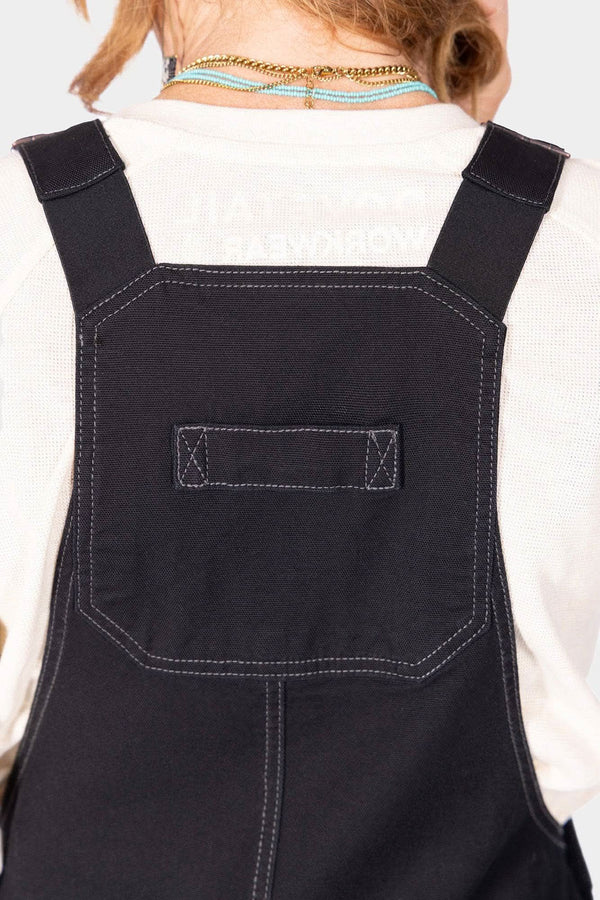Back view of a woman wearing Dovetail Workwear GO TO™ Stretch Canvas Overalls in Carbon Black, highlighting the reinforced knee and nested pocket details