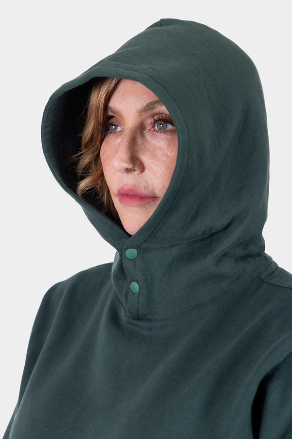 Woman wearing the Dovetail Workwear GO TO™ Hoodie in Lodge Green with the hood up, showing the snap neck closure and relaxed fit design