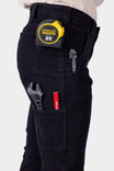 Side view of a woman wearing black Maven X Graphene Denim Pant by Dovetail Workwear, displaying multiple tool pockets and a 25' tape measure on the Hip Slot™