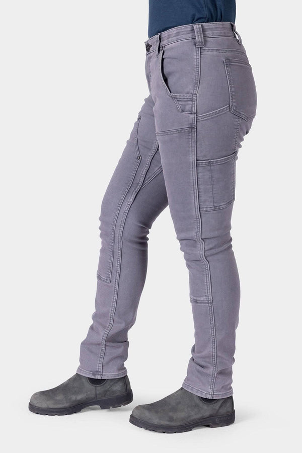 Side view of a woman wearing Dovetail Workwear's Maven X HOTSWAP™ Thermal Denim Pant in grey, featuring visible pockets and reinforced seams