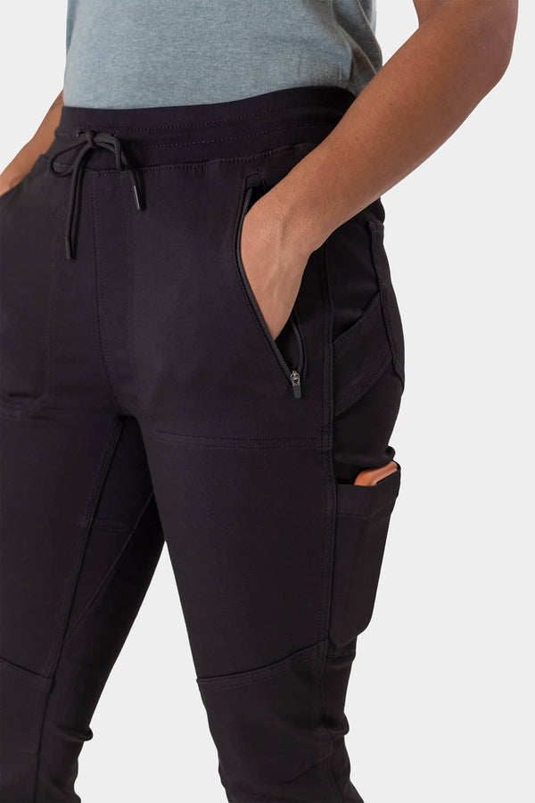 Close-up side view of a woman wearing the Dovetail Workwear Christa X DIY Pant in Black Performance Modal, highlighting the front zip pocket and nested side pocket details