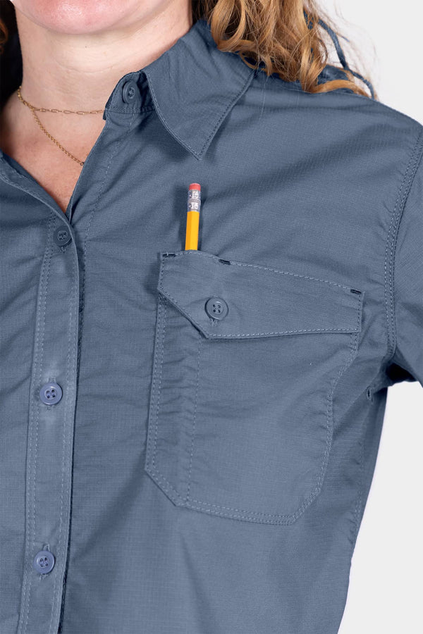 Detail view of the AJ COOLSWAP™ Work Shirt in Dovetail Blue, showing the buttoned chest pocket and pencil holder with a woman wearing a gold chain necklace