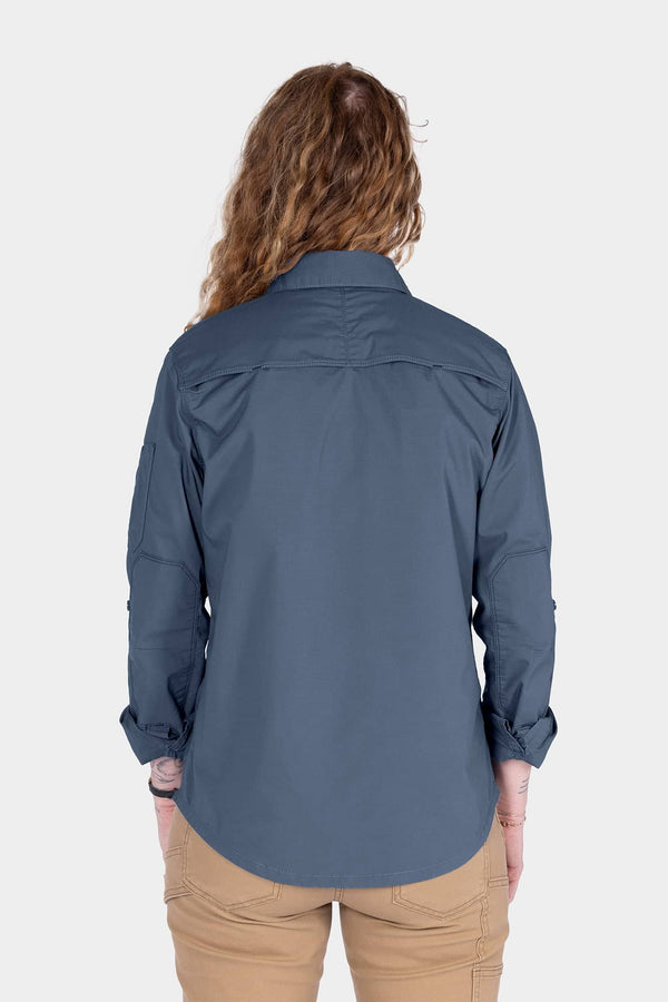 Back view of a woman wearing the Dovetail Workwear AJ COOLSWAP™ Work Shirt in Dovetail Blue with khaki pants, showcasing the back vent and shirt's relaxed fit