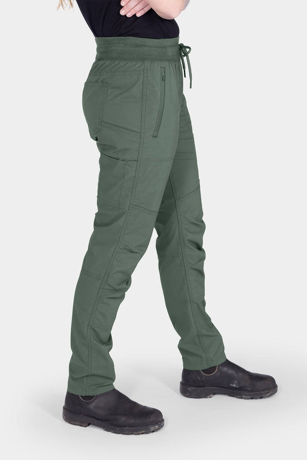 Side view of a woman wearing Dovetail Workwear's Christa X COOLSWAP™ Pant in Aventurine Green, showcasing the high-rise waistband, nested side pockets, and slim leg silhouette