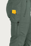 Side view of a woman wearing Dovetail Workwear's Christa X DIY COOLSWAP™ Pant in Aventurine Green, displaying multiple pockets including a yellow object in one of the pockets.