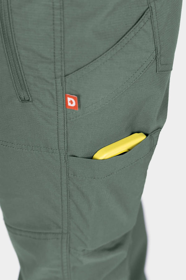 Detail shot of the Christa X DIY COOLSWAP™ Pant in Aventurine Green, showing the phone pocket with yellow pen and red logo patch