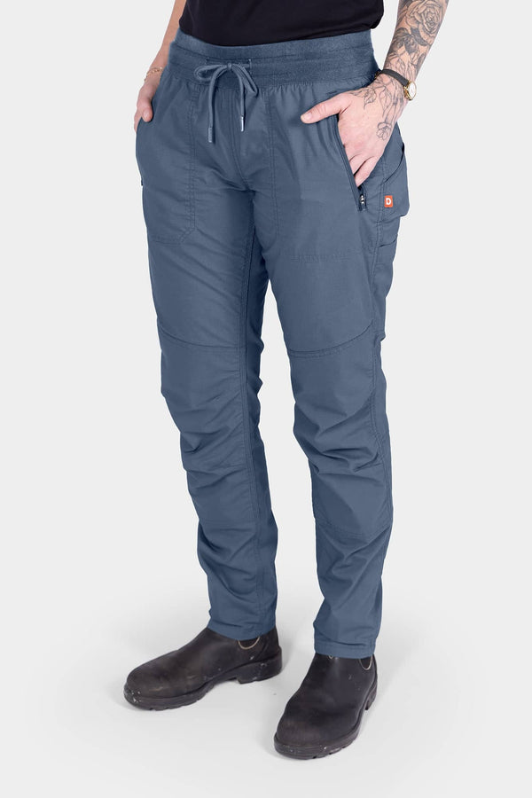 Woman wearing Dovetail Workwear's Christa X COOLSWAP™ Pant in Dovetail Blue, featuring COOLSWAP™ ripstop fabric, front zip pockets, and a high-rise waistband with drawcord