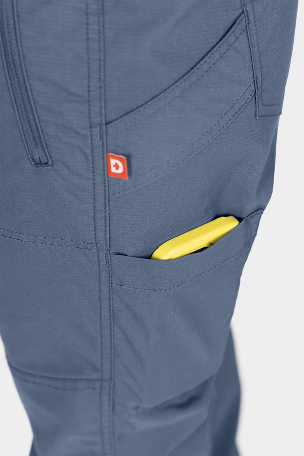 Detail shot of the Christa X DIY COOLSWAP™ Pant by Dovetail Workwear in Dovetail Blue, highlighting the phone pocket and logo label on the thigh
