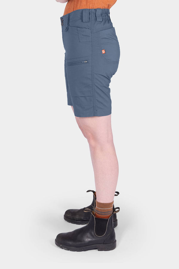 Side view of a woman wearing Dovetail Workwear's Compass COOLSWAP™ Cargo Short in Dovetail Blue, showcasing the bellowed zip cargo pockets and high-rise waistband design
