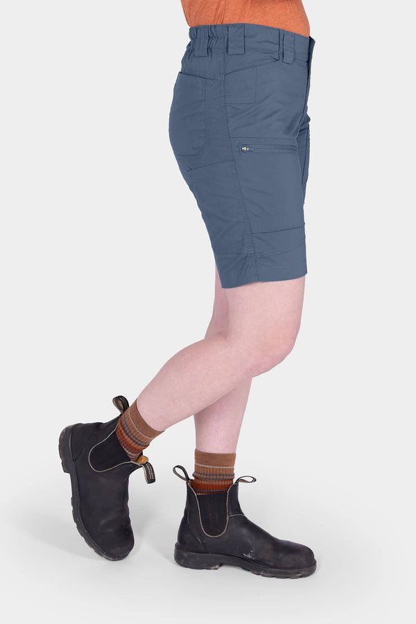 Side view of a woman wearing Dovetail Workwear's Compass COOLSWAP™ Cargo Short in Dovetail Blue, featuring bellowed zip cargo pockets and a high-rise waistband