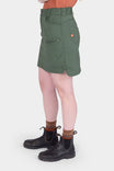 Side view of a woman wearing the Aventurine Green Compass COOLSWAP™ Cargo Skort by Dovetail Workwear, featuring visible bellowed zip cargo pockets and high-rise waistband