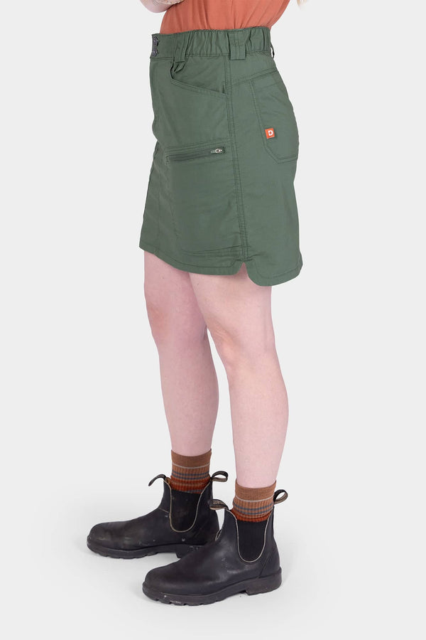 Side view of a woman wearing the Aventurine Green Compass COOLSWAP™ Cargo Skort by Dovetail Workwear, featuring visible bellowed zip cargo pockets and high-rise waistband