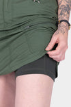 Detail view of a woman's hand on the Compass COOLSWAP™ Cargo Skort by Dovetail Workwear in Aventurine Green, showing the reinforced front pocket and stretch mesh undershorts